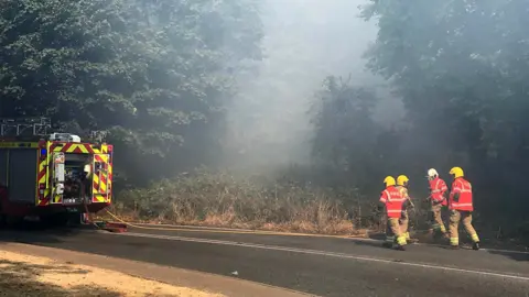Andrew Sinclair/BBC Fire crews walk through smoke on Mousehold Heath
