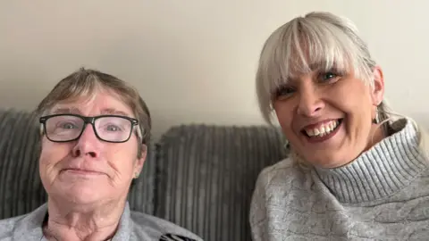 Mauren Wyatt, with glasses and grey top, alongside her daughter Ciara Burns who has grey hair and a grey jumper with longer collar.