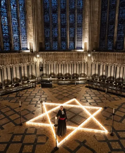 Danny Lawson / PA Media The Reverend Canon Michael Smith, Acting Dean of York, helps light six hundred candles in the shape of the Star of David, in the Chapter House at York Minster in York, part of York Minster's commemoration for International Holocaust Day