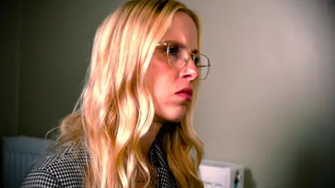 Nacoa A woman with blonde hair wearing glasses