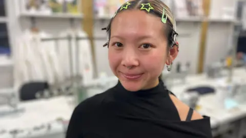 A woman wearing a black top, with brown hair and a number of hair clips, including some shaped as stars