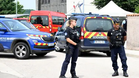 Gendarmes stand before police vehicles at the scene of the fatal stabbing in Nogent