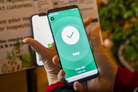 PA Media A bar worker holding a phone which is displaying a Covid-19 vaccine certificate