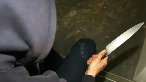 Katie Collins/PA Wire Man in a hoodie holding a knife