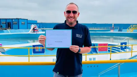 Medway Council Paul Johnston, Medway Sport and Leisure Manager, at The Strand Lido with a certificate presented by Historic Pools of England