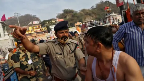 Reuters A police officer asks a devotee to leave after a dip