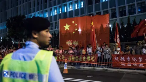 AFP A policeman keeps watch as pro-China supporters gather along a road during a visit by China's President Xi Jinping in Hong Kong on 29 June 2017