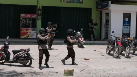 BBC Police fire warning shots outside a shop in Palu, Indonesia