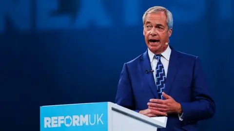 Reuters Nigel Farage speaks at a lecturn to the Reform UK audience. He is wearing a blue suit and a patterned tie.