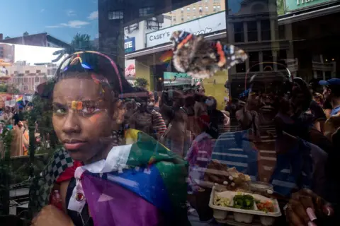 David Dee Delgado/Reuters A person looks out of a window at people participating in the 2023 NYC Pride Parade