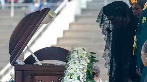 Getty Images Zimbabwe's former First Lady Grace Mugabe says a final farewell at the casket of late Zimbabwean President Robert Mugabe on September 14, 2019 during a farewell ceremony held for family and heads of state at the National Sports Stadium in Harare. - Mugabe, who died in Singapore on September 6, 2019 at the age of 95, left Zimbabwe deeply divided over his legacy with his country still struggling with high inflation and shortages of goods after decades of crisis.
