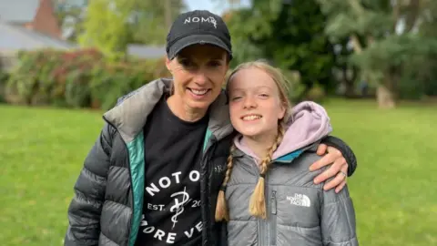 Sam Read/BBC Woman in blue cap and girl in grey jacket with pigtails.