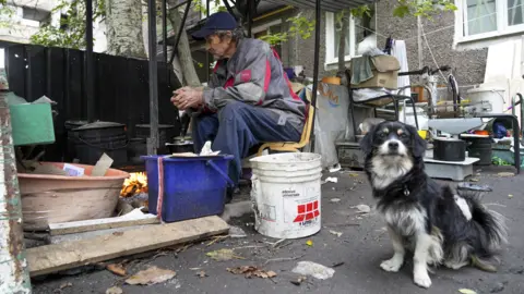 Getty Images A dog sits near a man keeping warm by a fire in Mariupol - 29 September 2022