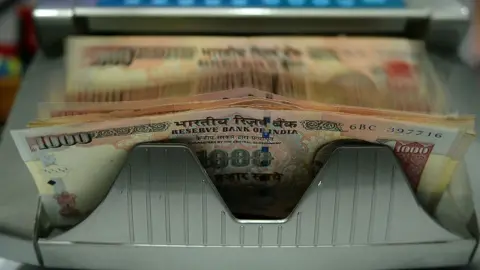 Getty Images An automatic machine counts Indian Rupee currency notes at a shop in Mumbai.
