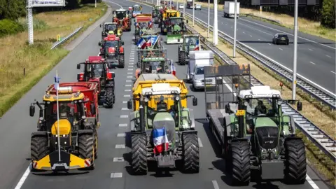 Getty Images Dutch farmers drive their tractors on the A35 motorway as they protest against the nitrogen plans causing delays due to the slow-moving of their vehicles near Bornerbroek, 28 July 2022