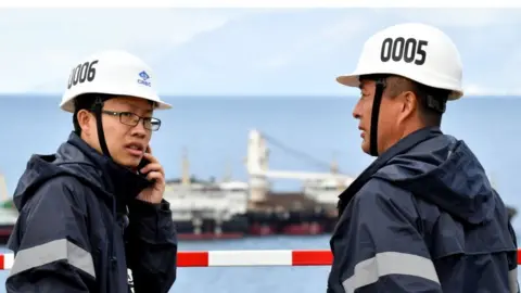 Getty Images A Chinese worker and engineer speaks on the phone next to one of his colleague, on April 11, 2019, in Peljesac