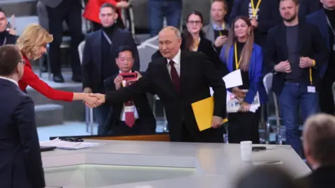 Getty Images Russian President Vladimir Putin enters the hall during his combined call-in-show and annual news conference