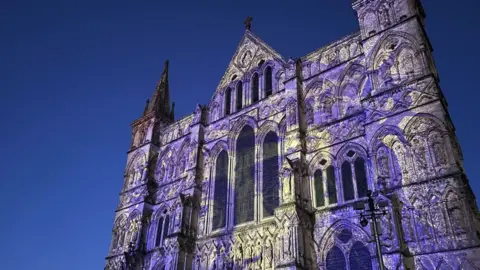 BBC Image of the Sarum Lights exhibition at Salisbury Cathedral. The building has blue and yellow patterns projected onto it.