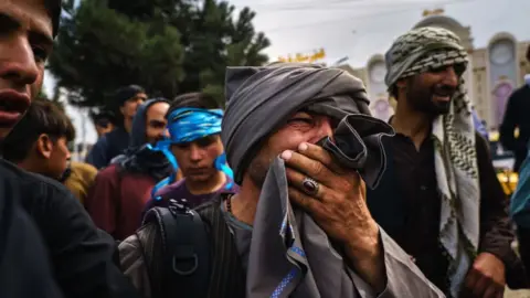 Getty Images A man cries as he watches fellow Afghans get wounded by Taliban fighters outside Kabul Airport