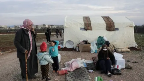 Reuters Earthquake survivor, Mahmoud Abd el-Shehiel, stands with his children outside tents erected for people affected by a devastating earthquake, in rebel-held town of Jandaris, Syria