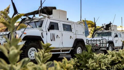 Getty Images Two white Armoured UNIFIL vehicles, with some green bushes in the foreground and blue skies in the background. 