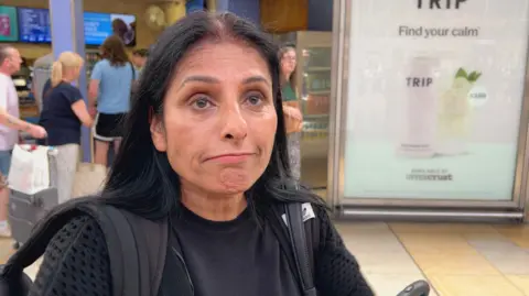 BBC/Harry Low Woman with black hair wearing two bags at railway station