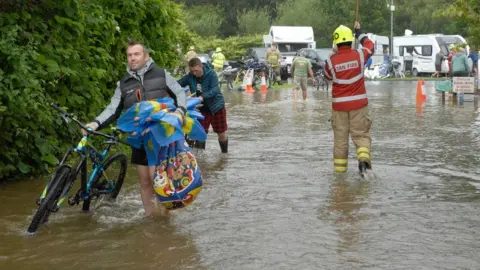 Malcolm Richards/Athena Pictures Firefighters help campers, carrying bikes from their motorhomes in Pembrokeshire