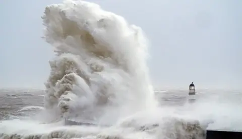 PA Media Huge waves crash against the lighthouse in Seaham Harbour