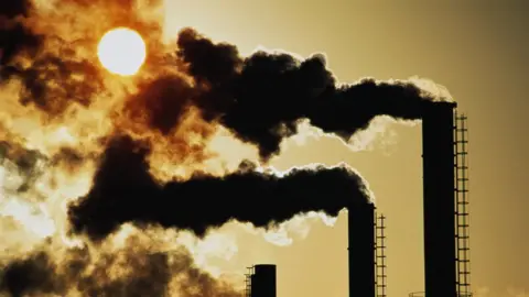Getty Images Smoke pluming out of 3 chimneys in front of hazy bright sun