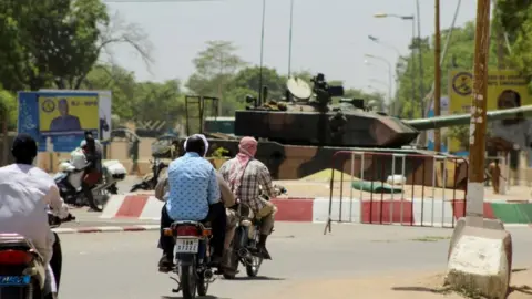 Reuters People riding on motorbikes past a tank near the presidential palace in N'Djamena, Chad
