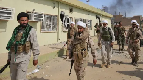 AFP Shia fighters from the paramilitary Popular Mobilisation force walk inside al-Nour district of Tal Afar, northern Iraq (23 August 2017)