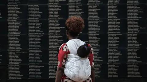 Getty Images A woman carrying her child looks at a memorial to victims of the 1994 Rwandan Genocide