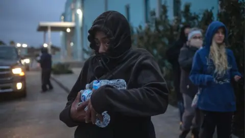 Reuters A woman carries bottled water she received from a shelter after record-breaking temperatures in Galveston, Texas, 18 February 2021