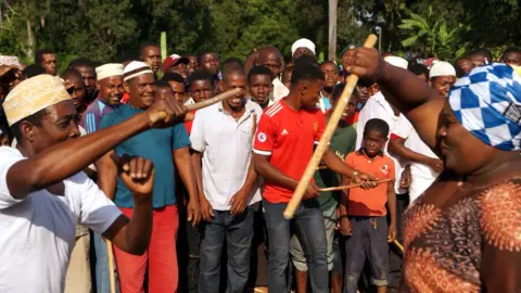 Catherine Tilke Men and women line up and take turns to 'fight' with batons while a band plays folk music