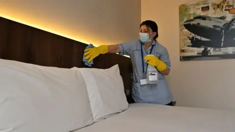 Getty Images A member of the cleaning staff cleans surfaces as she prepares a room for a guest at the St Giles Hotel, near Heathrow Airport
