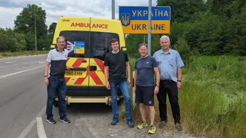 Steve Challen Four men stand at the back of an ambulance at the Ukraine border