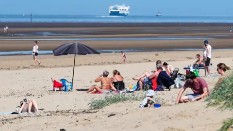 PA Media People relax on Crosby Beach on the Merseyside