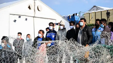 EPA Migrants stand behind a fence at Karatepe refugee camp on Lesbos island, Greece, 29 March 2021