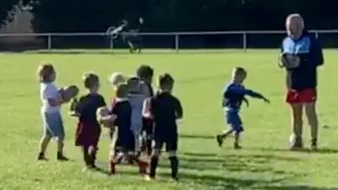 Ian Griffiths Young children at rugby training, with a motorbike doing a wheelie in the background