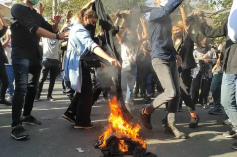 Getty Images A woman burns her headscarf on a bonfire at a protest in Tehran, Iran (1 October 2022)