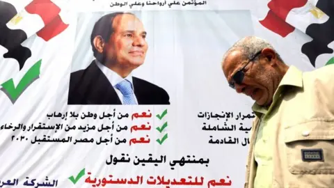 Reuters A man walks in front of a banner reading, "Yes to the constitutional amendments, for a better future", with a photo of the Egyptian President Abdel Fattah al-Sisi before the approaching referendum on constitutional amendments in Cairo, Egypt on 16 April 2019.