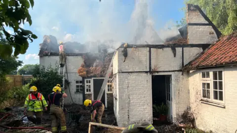 BBC A fire in thatched roof of house in Urchfont with firefighters in action