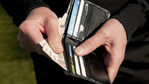 Getty Images A man holding his wallet and getting money out