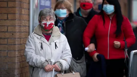 Getty Images A woman wearing a Welsh flag face mask stands in a queue for vaccine