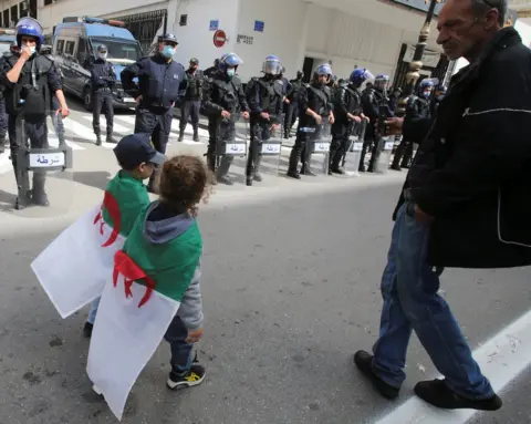 Reuters Children wearing Algeria's national flag walk past as police officers stand guard during a protest.