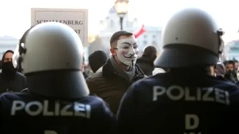 Getty Images Man in anonymous mask surrounded by police in Austria