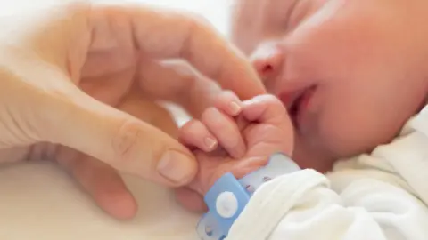 Getty Images Carer holds the hand of a baby