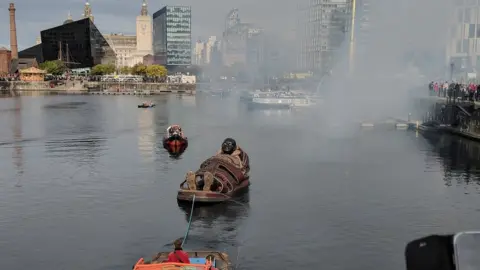 Giant Spectacle boy giant in boat pulled through dock by boat