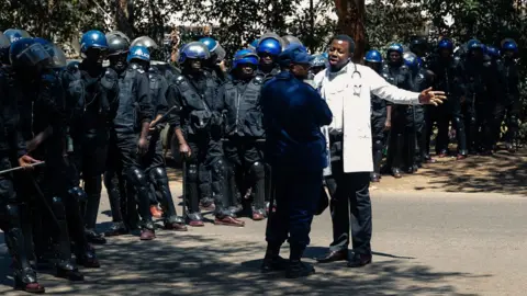 Getty Images A doctor speaks with the anti-riot police for a safe passage during a protest of doctors and medical staff for the safe return of Dr Peter Magombeyi, the leader of the Zimbabwe Hospital Doctors Association (ZHDA,) on September 18, 2019, in Harare. - Hundreds of Zimbabwean doctors and nurses marched in Harare on September 16, 2019, to protest the suspected kidnapping of a doctors' union leader by security forces for organising a slew of strikes. Peter Magombeyi has been missing since September 14, 2019, night, after sending a WhatsApp message saying he had been "kidnapped by three men", according to the Zimbabwe Hospital Doctors Association (ZHDA).