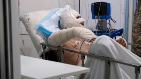 Reuters A Lebanese soldier speaks to a man injured in a petrol tank explosion in Akkar at a hospital in Beirut (15 August 2021)